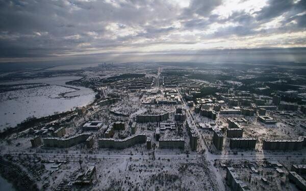 Aerial view of abandoned Pripyat under snow, showing rows of apartment blocks and empty streets beneath an overcast sky